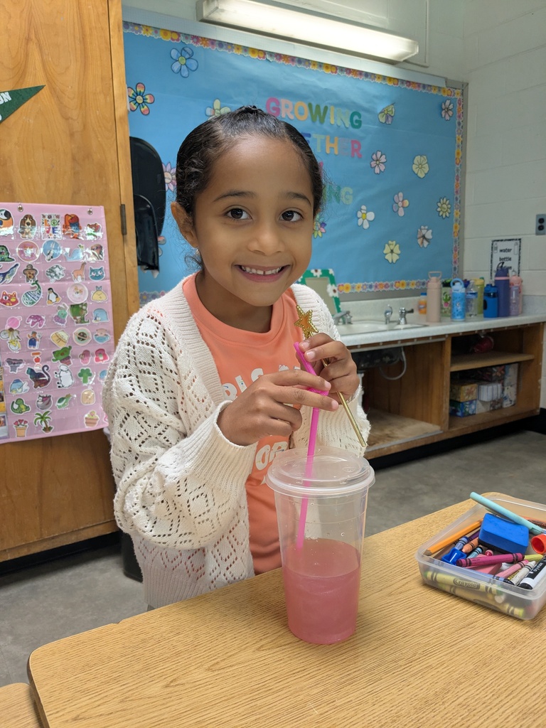 Student smiling drinking her pink drink through a straw in her classroom.