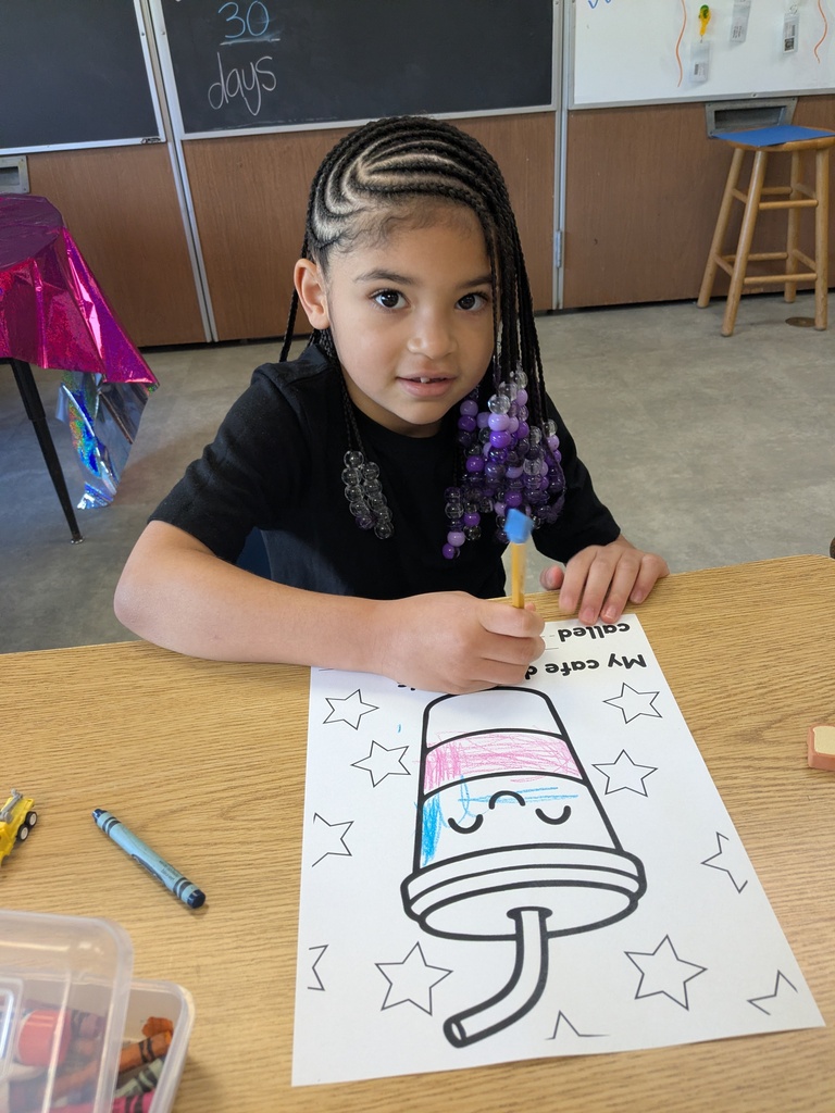 A child with braided hair sits at a desk coloring a picture of a popsicle with markers.