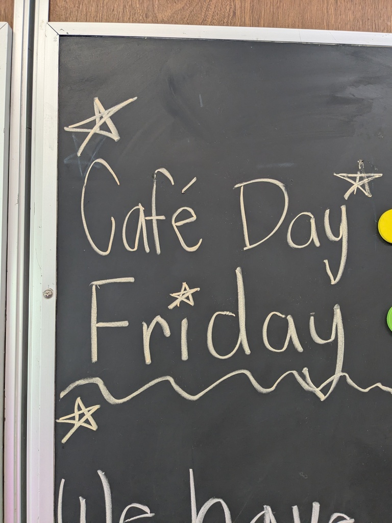 Black chalkboard with white chalk text. It reads "Cafe Day Friday" with stars and wavy lines.