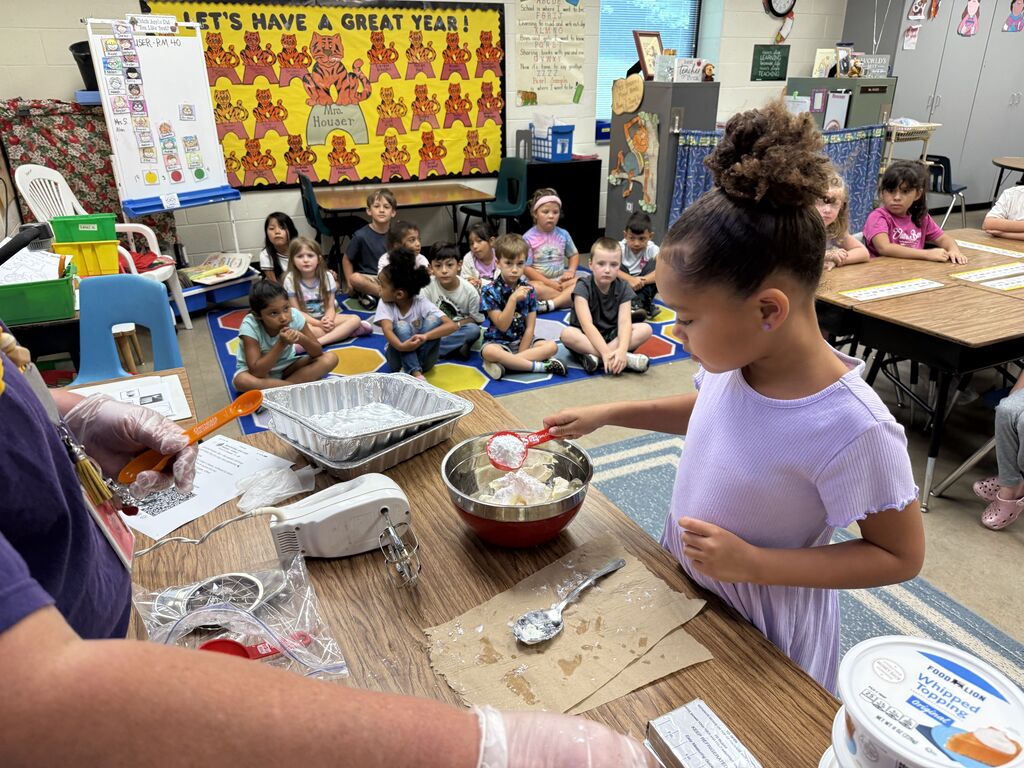 A child in a purple shirt helps an adult mix ingredients in a bowl at a table.