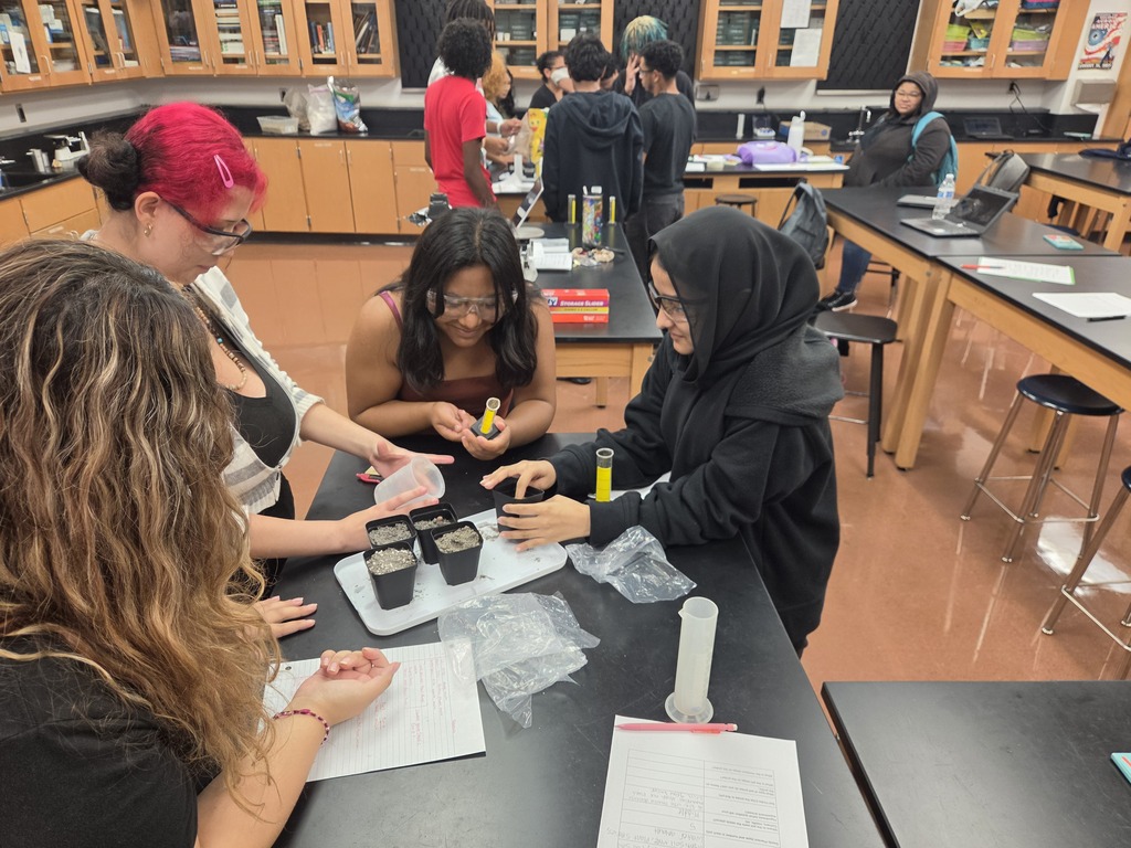 A group of individuals in a science lab, working at a table with plants and papers.