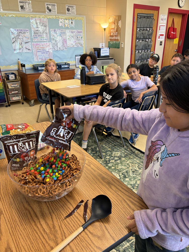 A child in a purple long-sleeve shirt holding a bowl of snacks and a spoon in a classroom.