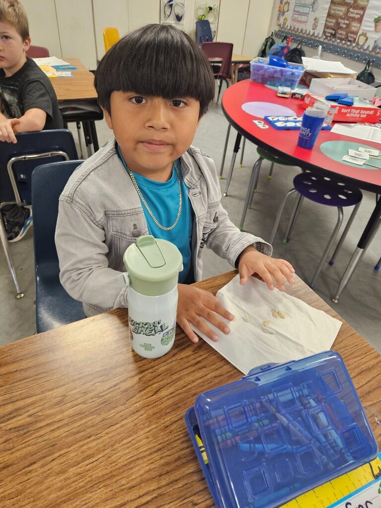 Child at a desk, holding a tissue, with a reusable water bottle on the table.