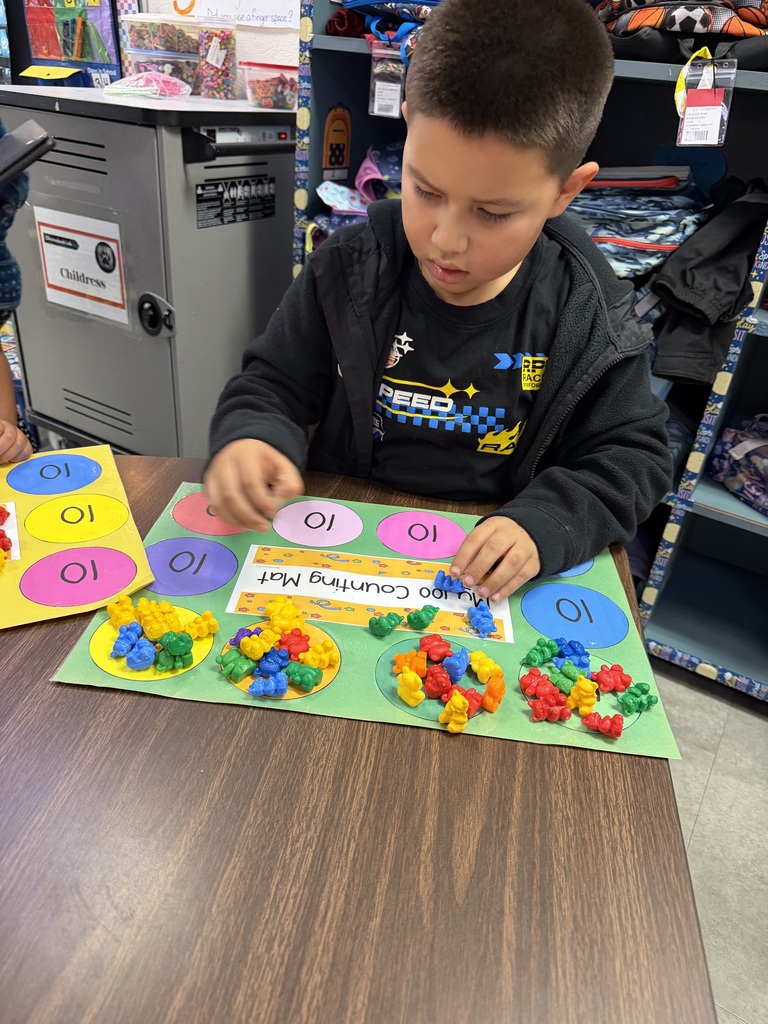Child seated at a table, playing with colorful beads on a colorful board, in a classroom.