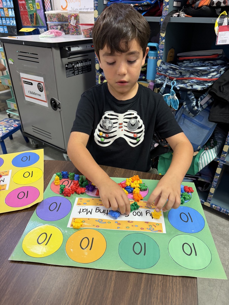 A child, wearing a black T-shirt, is playing with colorful beads on a table in a classroom.