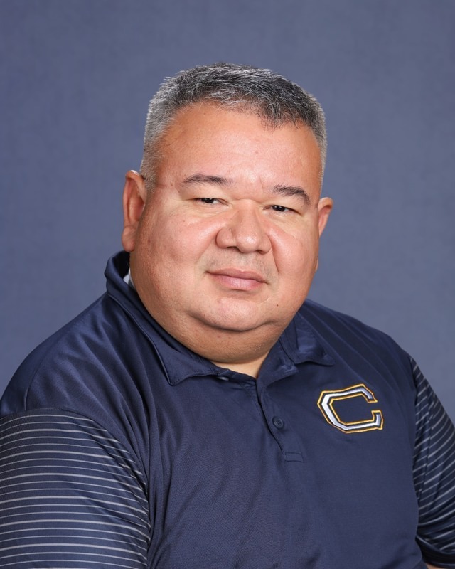 A man with gray hair wearing a blue polo shirt with a logo, smiling at the camera.