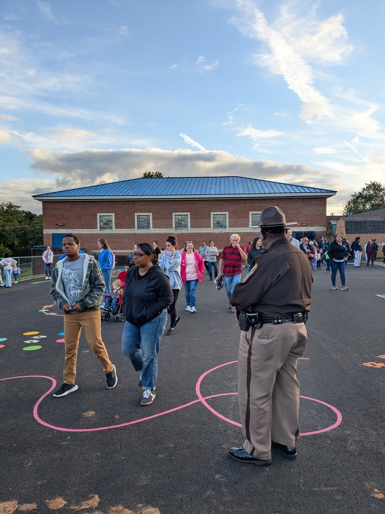An officer stands in a parking lot with colorful chalk designs. People walk around, and a building is in the background.