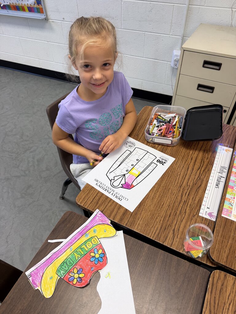 A young girl in a purple shirt sits at a table, working on a coloring activity.