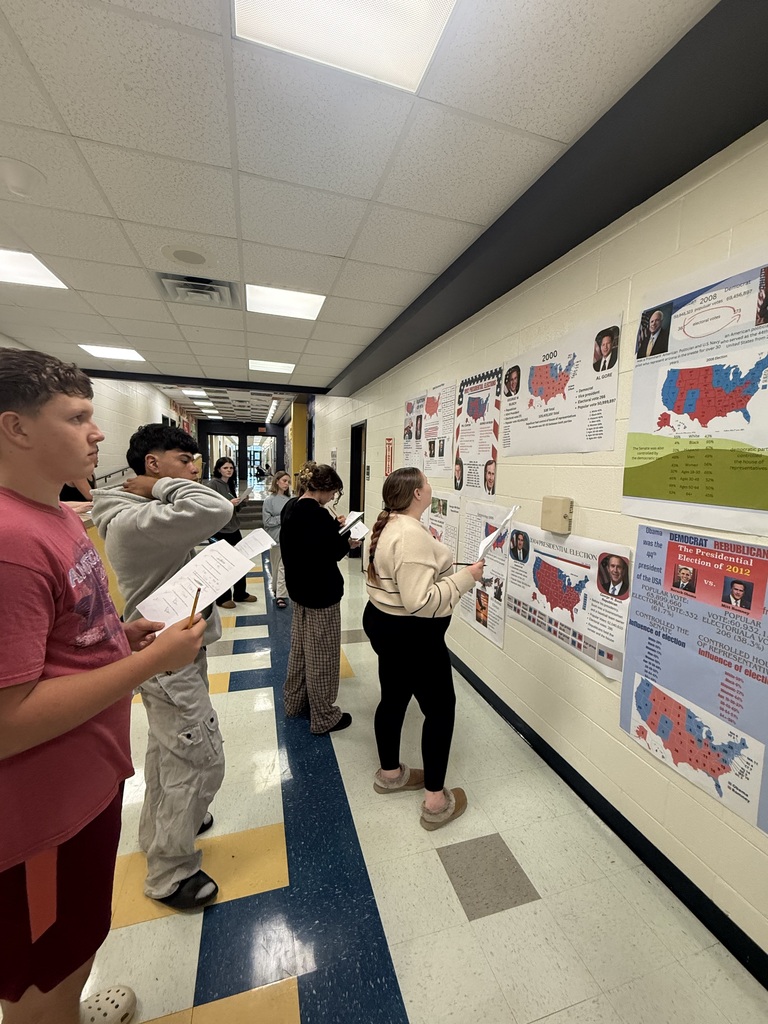 Students stand in a hallway examining posters with blue and red maps of the USA