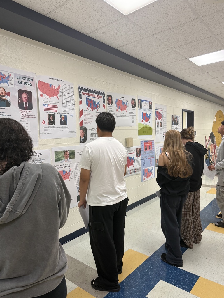Students stand in a hallway examining posters with blue and red maps of the USA