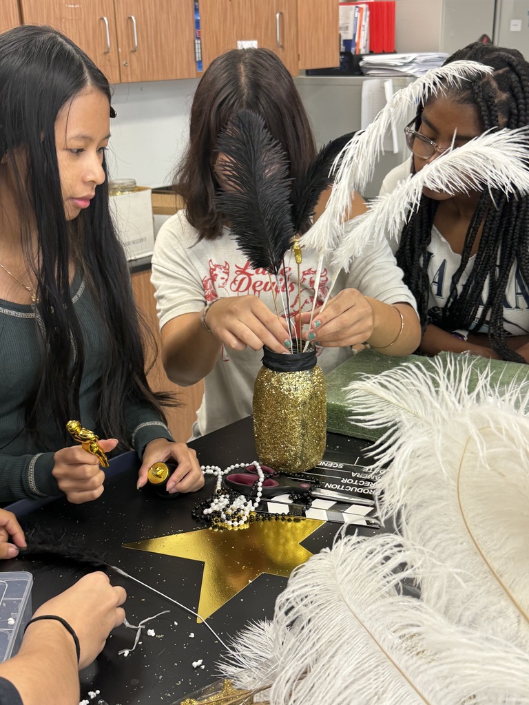 Several students work at a table, arranging feathers and other materials into a decorative centerpiece.