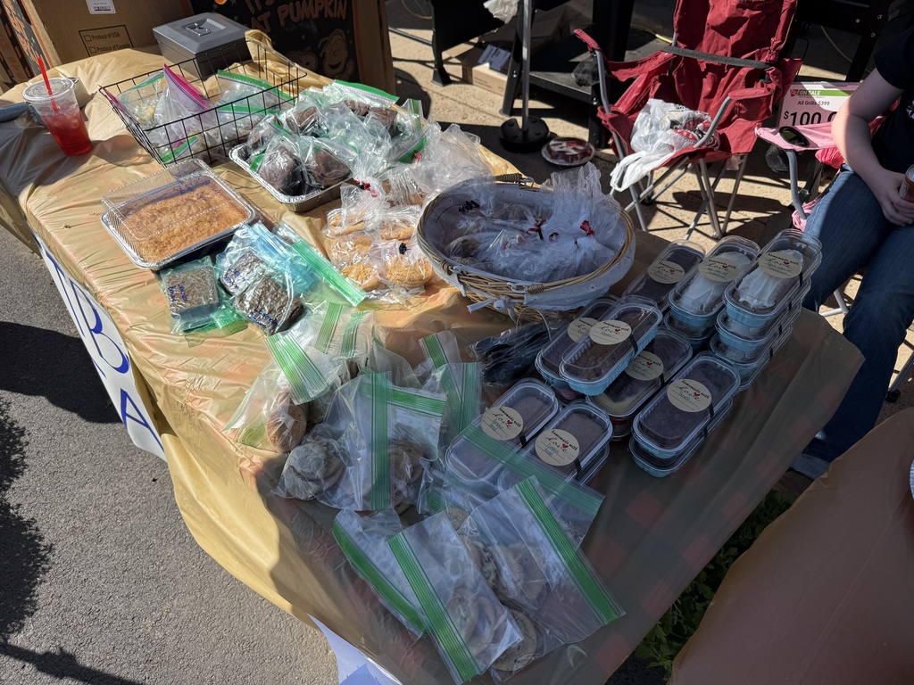A table covered with a yellow cloth displays packaged food items and containers, along with other items.