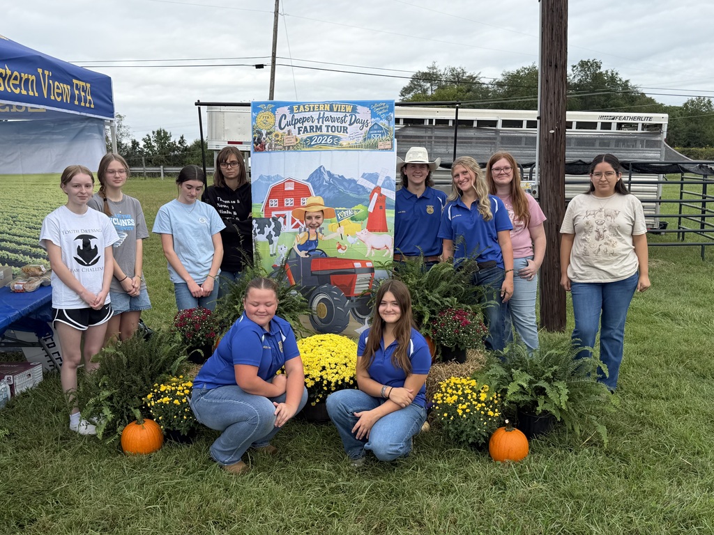 A group of people in matching blue uniforms pose with plants and pumpkins in a field.