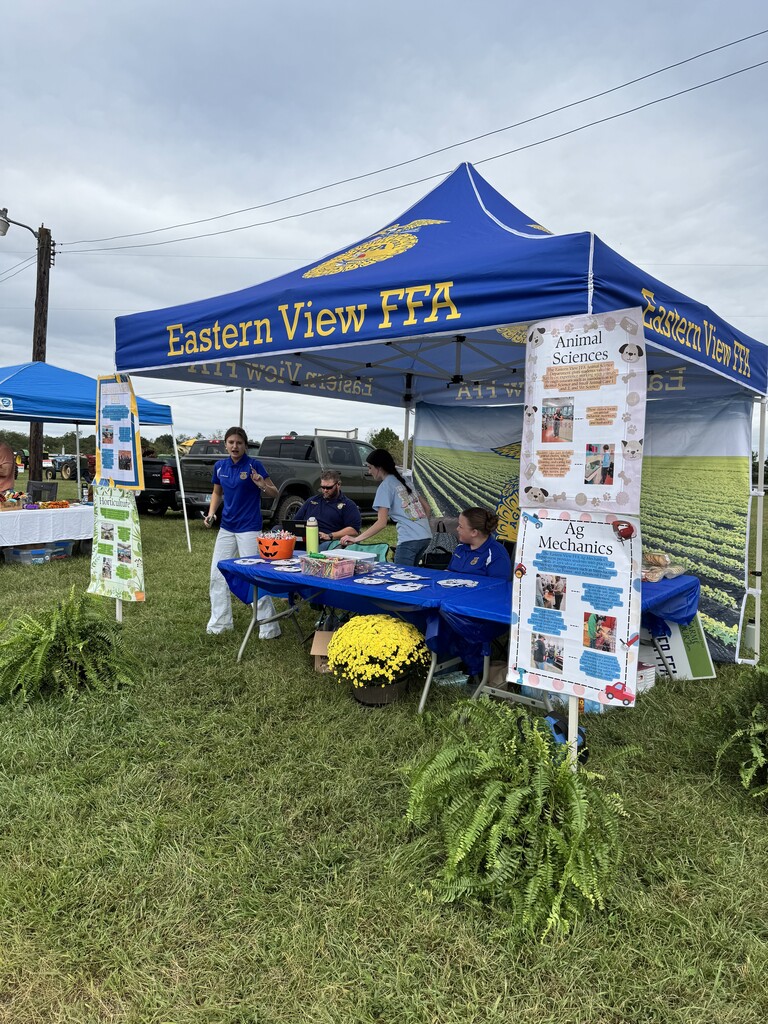 A blue tent with "Eastern View FFA" displays items and a person inside a field.
