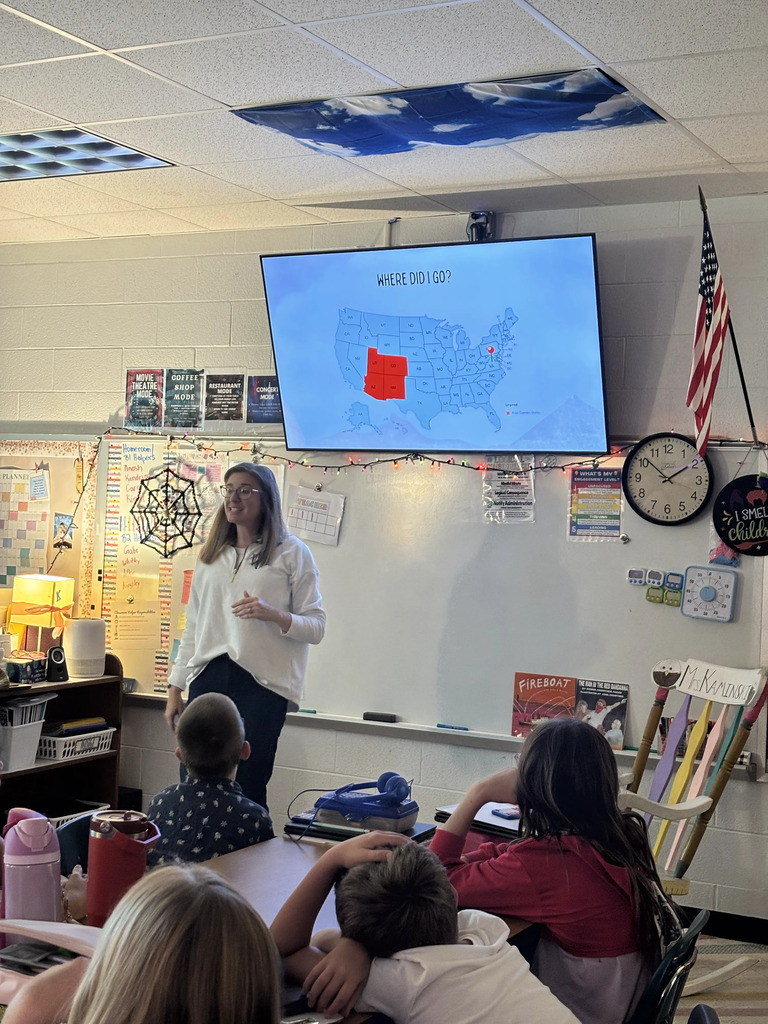 Teacher with a map of the US on the screen in a classroom with students seated in chairs.