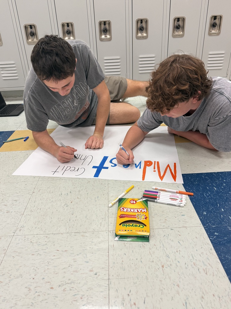 Two young people are lying on a floor, writing on a large white sheet with markers.