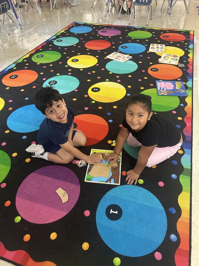 Two children on a colorful carpet with circles, engaging with a book and number cards.