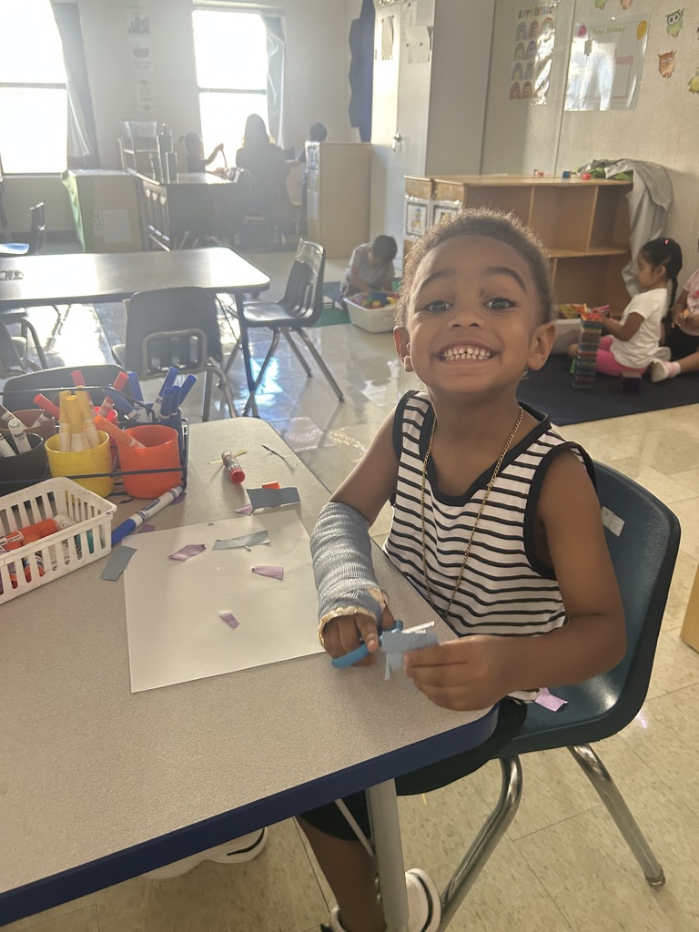 A smiling child in a striped shirt sits at a table, wearing a cast on one arm.