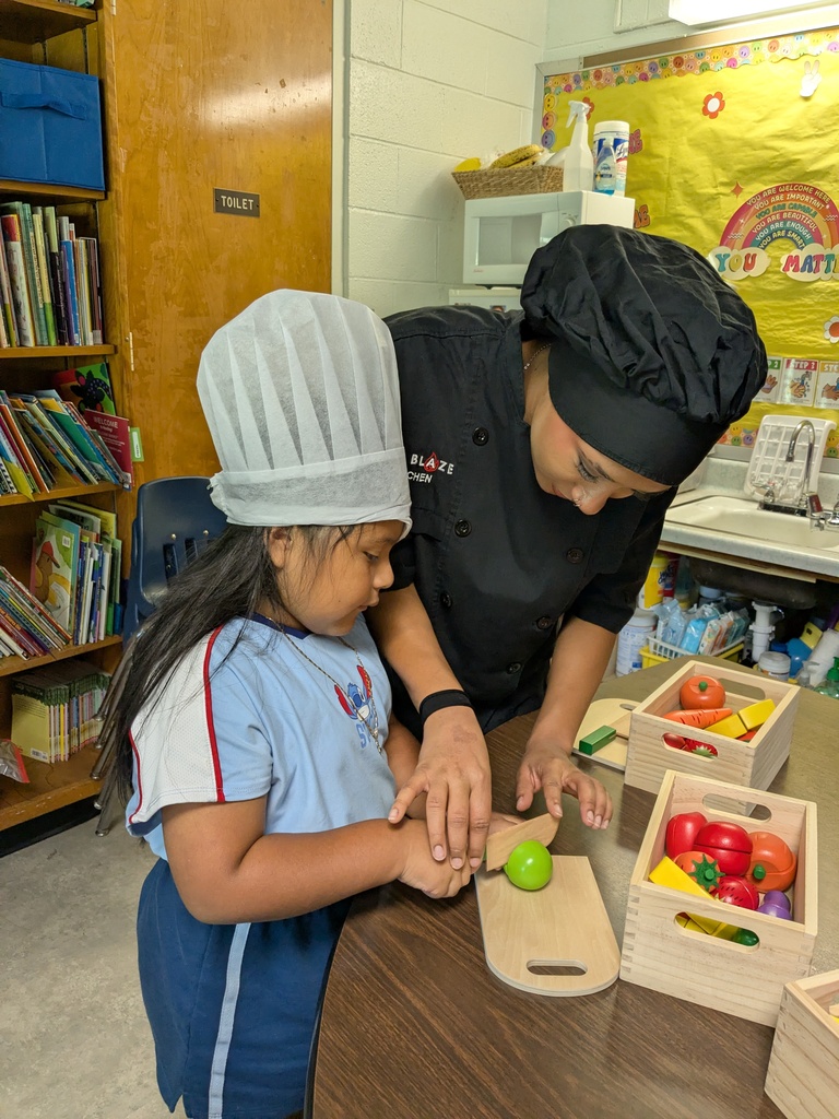 A chef and a young child in a kitchen setting, with the child holding a green apple.