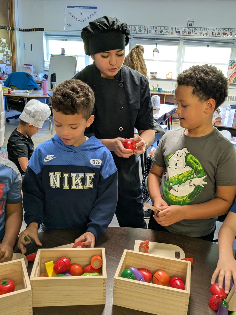 Children examine apples in a classroom setting; one child holds an apple, and another holds a knife.