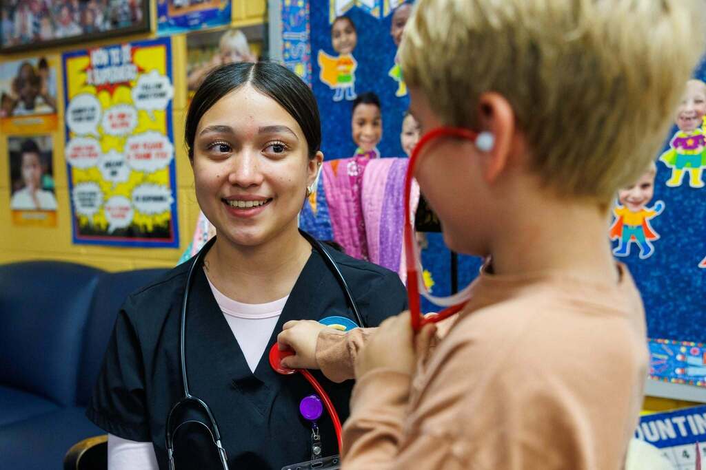 CTEC Medical Assistant student smiles as a first grader uses a stethoscope during the Day of Career Exploration.