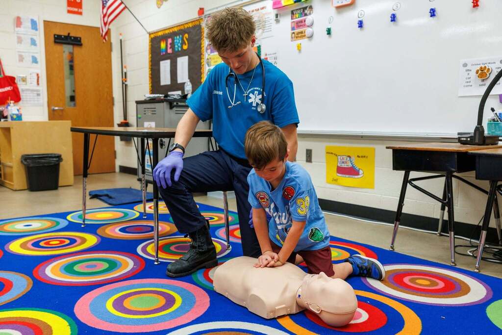 CTEC EMT student guides a first grader practicing CPR chest compressions on a manikin during the Day of Career Exploration.