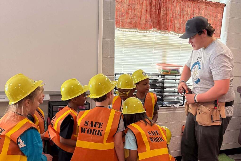 CTEC Carpentry student works with first graders wearing hard hats and safety vests during a hands-on career activity.