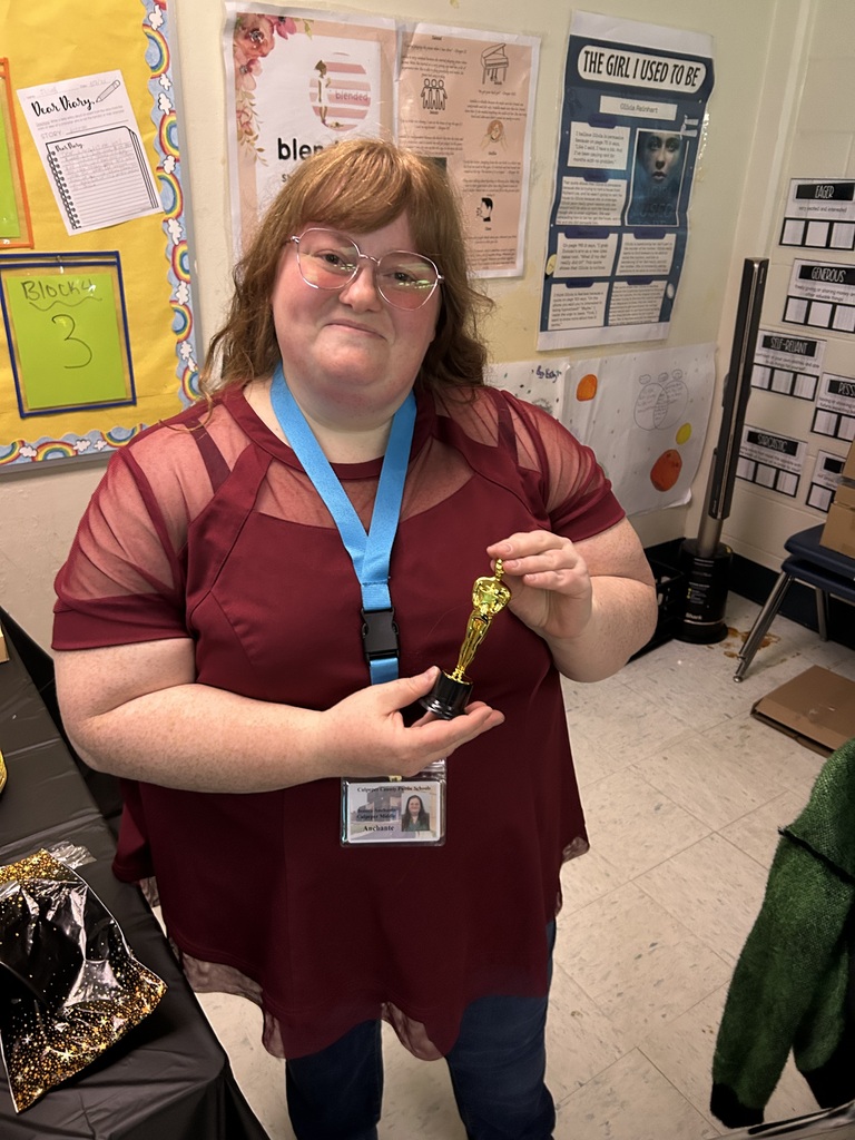 A 6th grade English teacher smiles while holding a small gold trophy in her classroom during the sixth-grade published-author celebration.