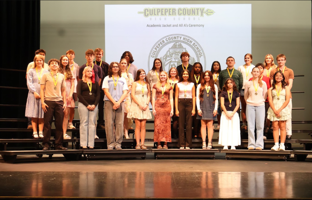 A group of students wearing medals stand on a stage under a screen displaying "Culpeper County".