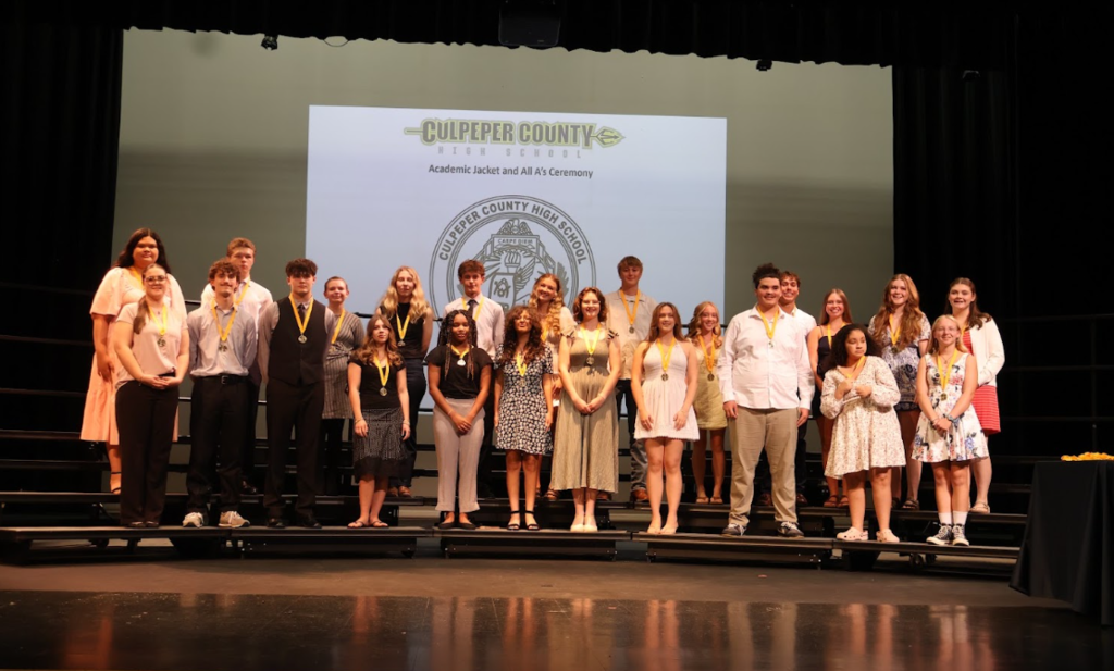 Group of young people on stage, some with medals, standing in front of a projector screen.