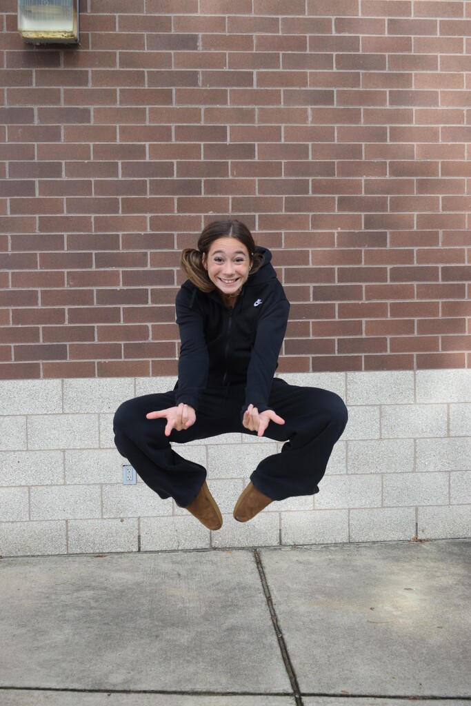 A person jumps in the air in front of a brick wall with a white border.