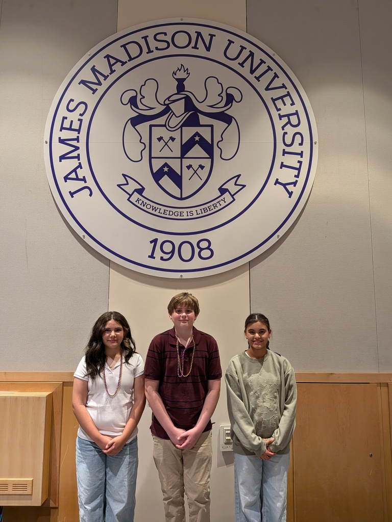 Three students stand beneath a large James Madison University seal featuring the university crest and the words “Knowledge is Liberty.”