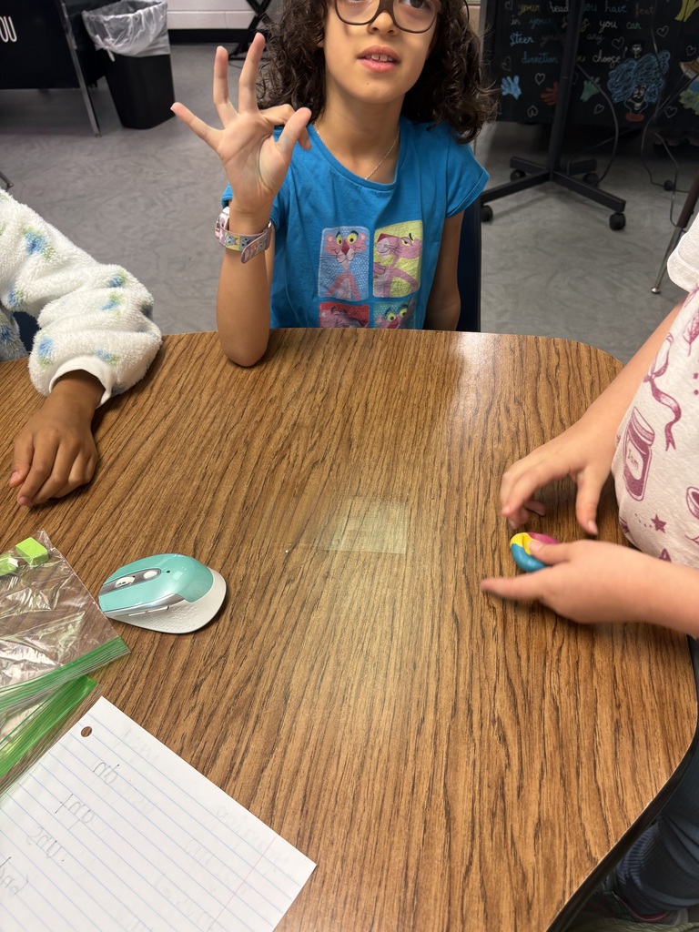 A girl in glasses seated at a table, using her hands to count, with a mouse and paper nearby.