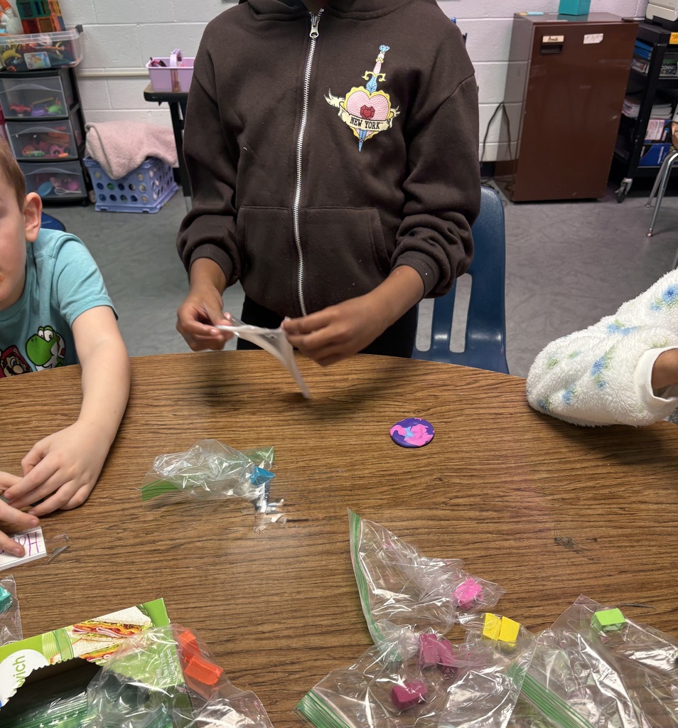 A boy and a girl are seated at a table with plastic bags containing colorful items.