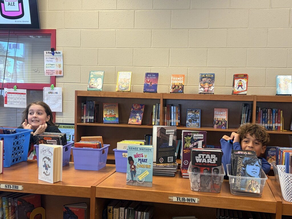 Two children seated in front of a bookcase with a variety of books on display.