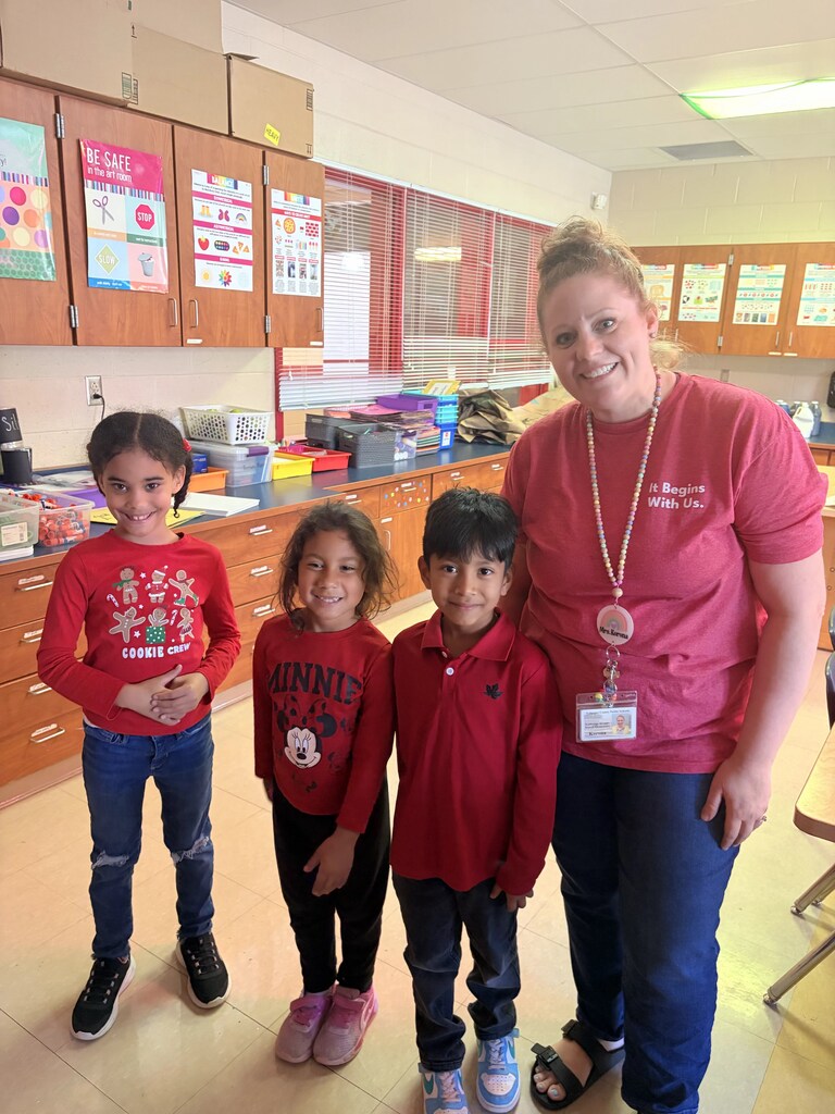 Woman with a lanyard stands with three children in a classroom with a tiled floor.
