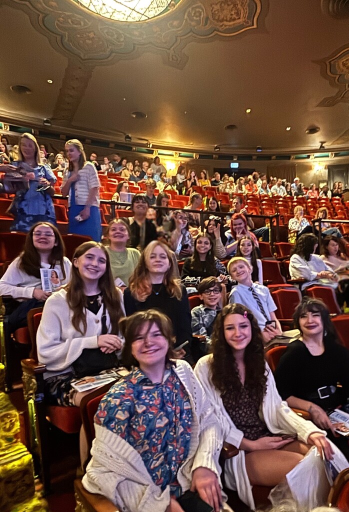 A group of people seated in theater chairs, some looking at the camera, others looking away.