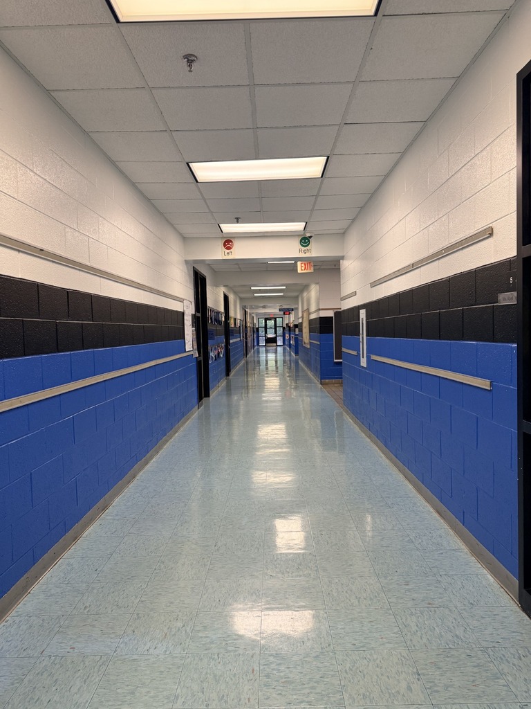 An empty hallway with white and blue walls and a light blue floor. There are doors on either side and lights on the ceiling.