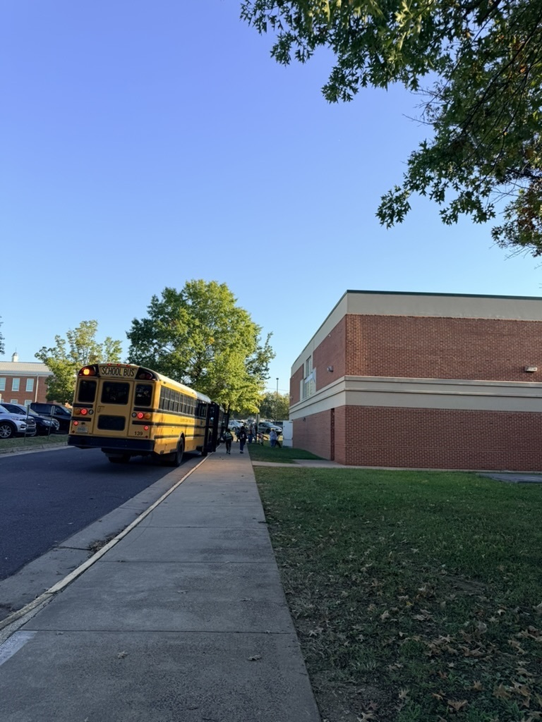 A yellow school bus is parked on the side of a road, next to a building. Students are boarding the bus.