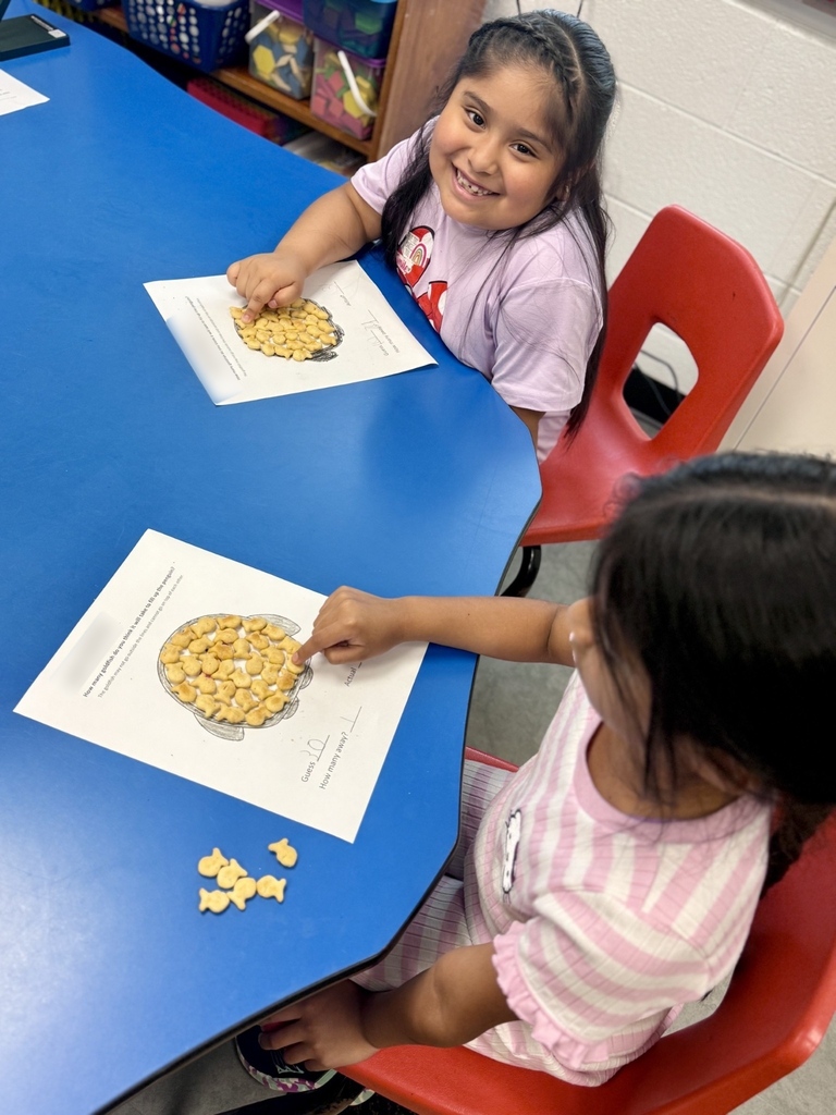 Two young girls sitting at a blue table, each with a piece of paper and a bowl of crackers.