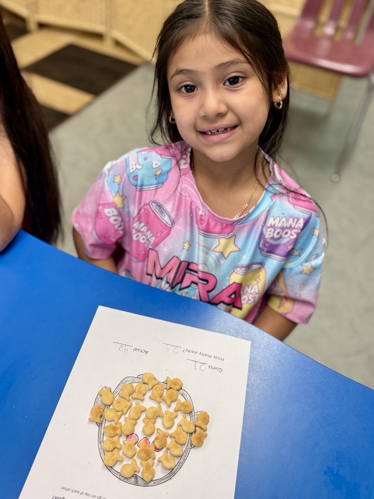 A young girl in pink pajamas sits at a blue table with a food-related worksheet.
