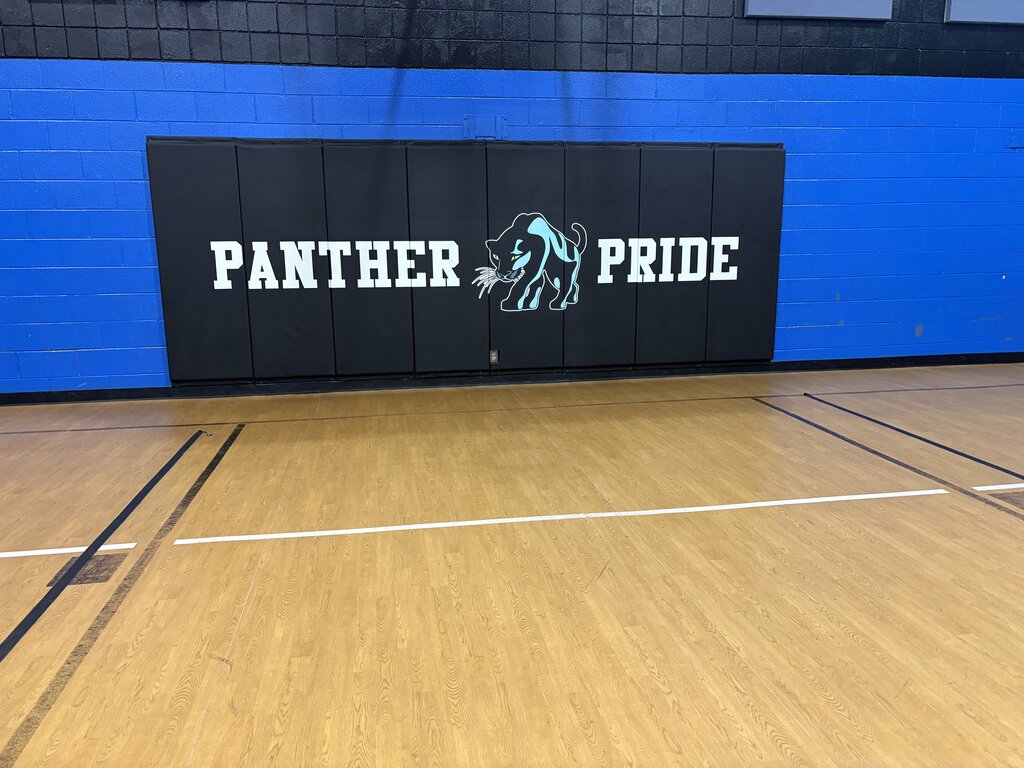 An indoor court with wooden floor, blue wall, and a large sign reading "Panther Pride" with a panther logo.