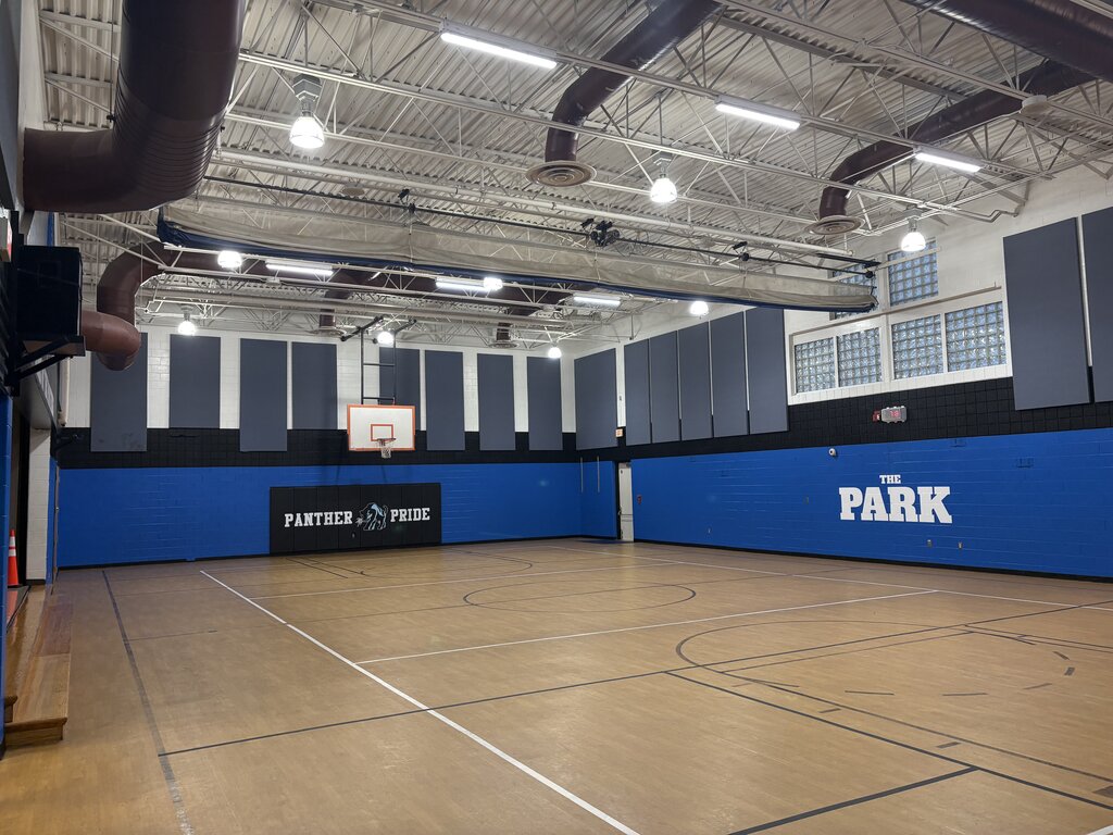 An indoor basketball court with blue walls and white lines, no people visible, and a black sign reading "Park" on the wall.
