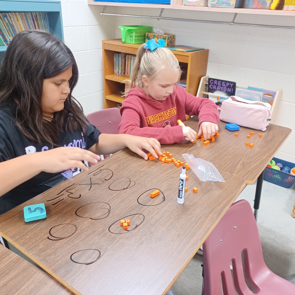 Two children sitting at a table, using orange beads to solve a math problem.