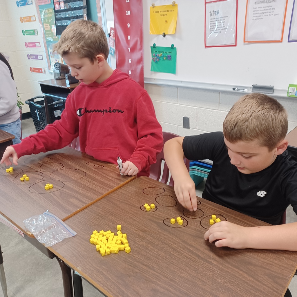 Two children playing a game of marbles on a table inside a classroom.