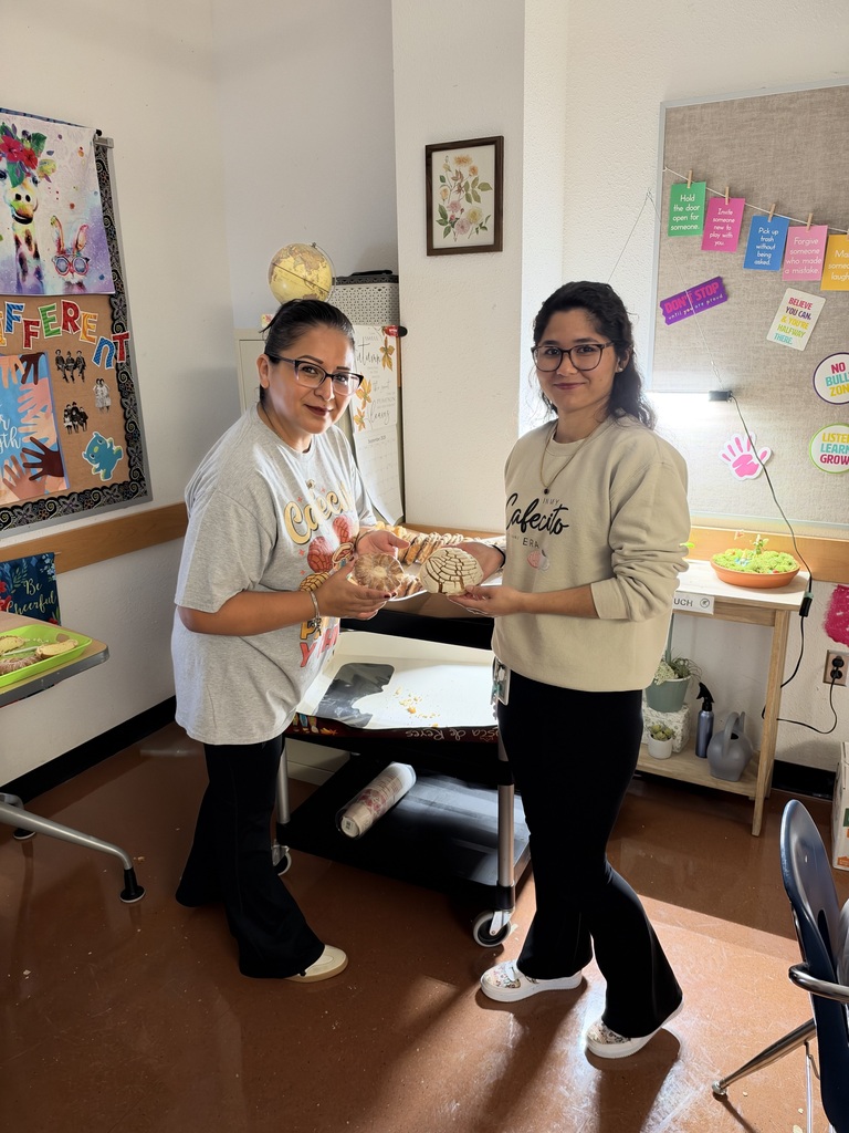 Two people in a room, holding bread. One wears glasses and a white shirt, the other a beige top.