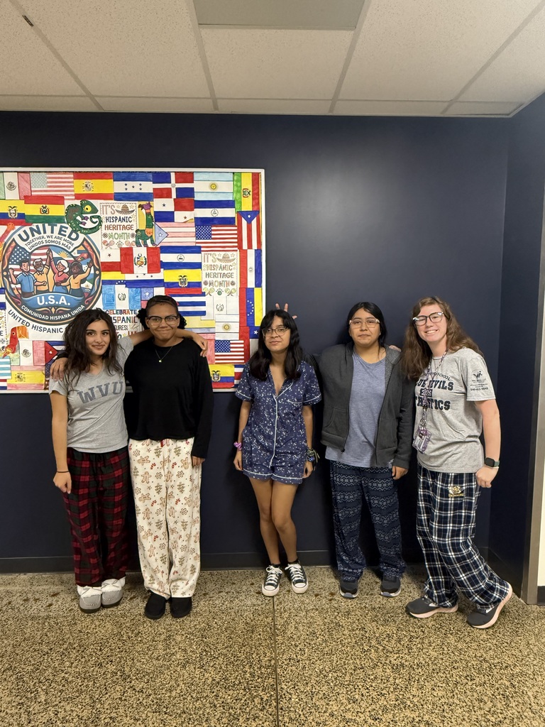 Five people wearing pajamas, two with floral and three with plaid, standing in front of a wall with a colorful flag mural.