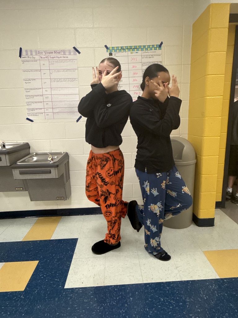 Two people in pajamas and slippers covering their eyes in a hallway with blue and yellow floors.