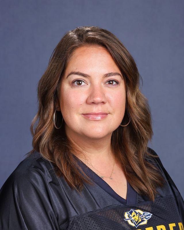 A woman with brown hair wears a navy blue jersey with the word "Raiders" on it.