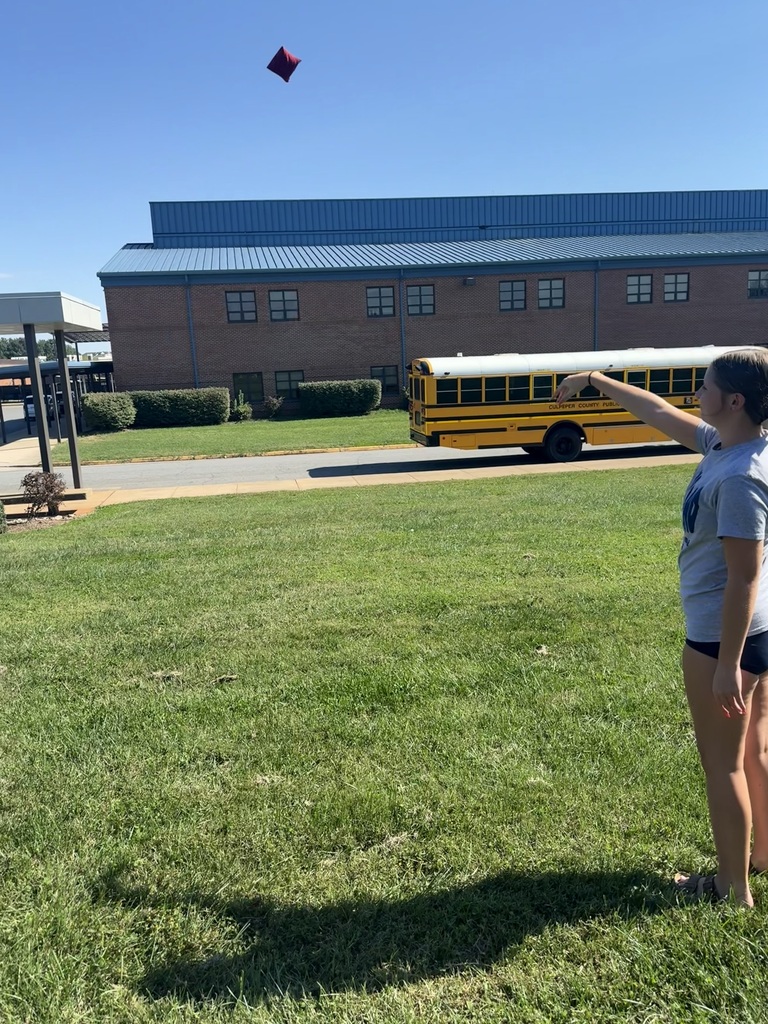 A person on a lawn throws a red object into the air. A school bus drives by in the background.